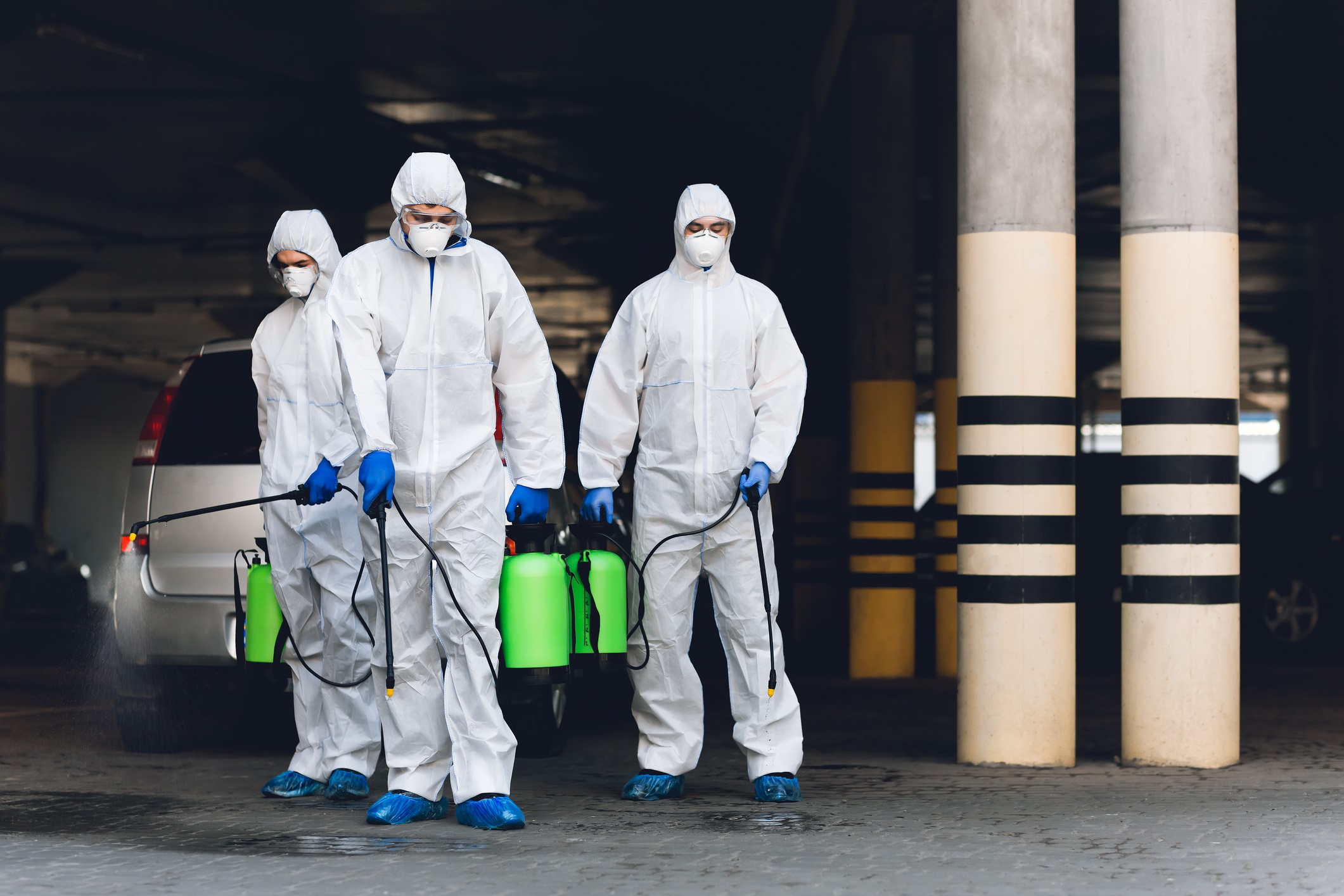 Medical workers in hazmat suits holding spray bottles with disinfecting chemicals