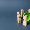 Wooden figures around green glass globe on grey background