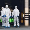 Medical workers in hazmat suits holding spray bottles with disinfecting chemicals