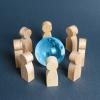 Wooden figures surrounding a blue glass globe. Concept of cooperation and collaboration of people and countries around the world