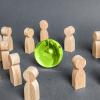 Wooden figures around a green glass globe signifying cooperation and collaboration of people around the world