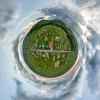 Little planet view of village houses and distant green cultivated agricultural fields with growing crops on bright summer day
