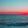 Crimson dawn. Clean energy offshore wind farm turbines on the ocean horizon. Beautiful red sky morning sunrise. New age environmental peaceful landscape scene.