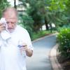 Elderly gentleman in white shirt having difficulties with extreme heat, high temperature, wiping sweat from face
