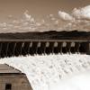 Black and white view from one side of the wall of famous Gariep Dam near Norvalspont in South Africa with open spillway and picturesque landscape in the background.