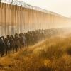 Line of people walking next to a high border wall