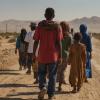 A group of refugees walk along a dusty desert road in search of a better life 