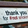 Sign encouraging non-smoking on a bench in a public outdoor area at a park
