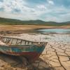 A weathered and empty reservoir or lake bed that has dried up due to prolonged drought, with cracks in the earth and abandoned boats lying on dry land AI generated 
