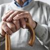 Close up details of the folded hands of an elderly man resting on a walking cane