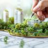 The image depicts a hand drawing on a blueprint with a detailed miniature model of a sustainable city.