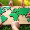 People collaborate assembling green world map puzzle on grass.