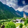 A beautiful church sits amongst mountains, green fields and forests in Heiligenblut, Austria 