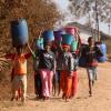 African kids carrying water in a dry landscape